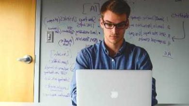 tahtanın önünde bilgisayara bakan gözlüklü erkek